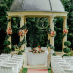 Vue en perspective des chaises de part et d'autre d'un tapis qui mènera les fiancés vers la pergola pour célébrer le mariage.