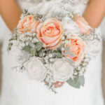 Mariée photographiée avec son bouquet de roses blanches et saumons en premier plan.