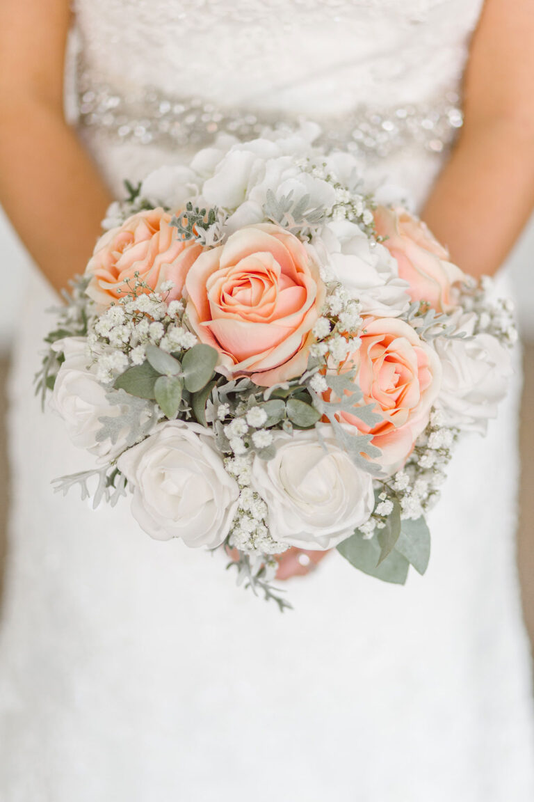 Mariée photographiée avec son bouquet de roses blanches et saumons en premier plan.