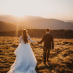 Photo sépia d’un couple récemment marié, vu de dos dans une prairie avec des montagnes en arrière-plan