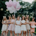 Photo de groupe des amies de la mariée tenant un bouquet de ballons roses et blancs.